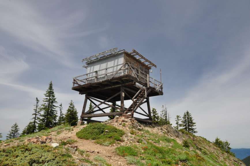 A cabin on stilts sits on a mountaintop with open sky behind.
