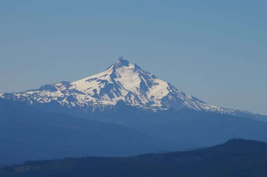 A snowy volcanic mountain with a sharp peak beyond ridgelines in the foreground.