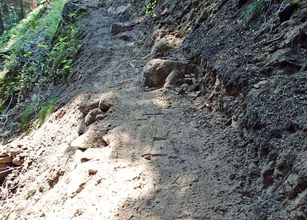 A trail on a steep hillside with boulders on the downhill side.