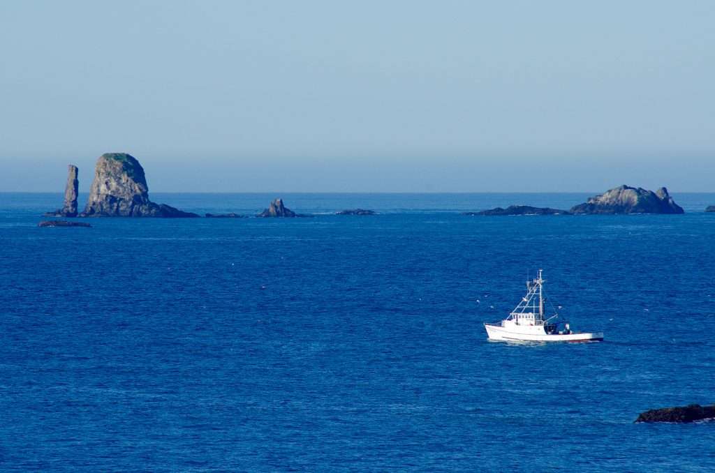 A row of rock islands in a blue ocean with a fishing boat passing in front.
