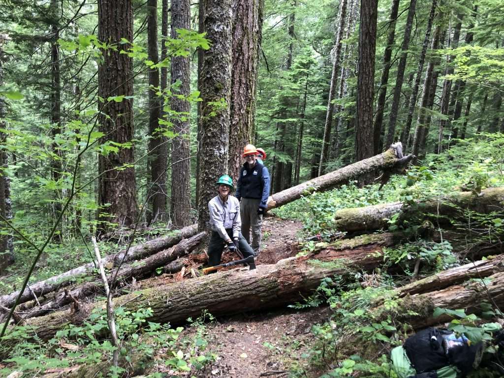 Three workers with a log across a trail in front of them and another across the trail behind them.