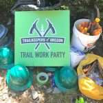 A TKO "Trail Work Party" sign surrounded by hardhats, gloves, loppers, and other trail tools.