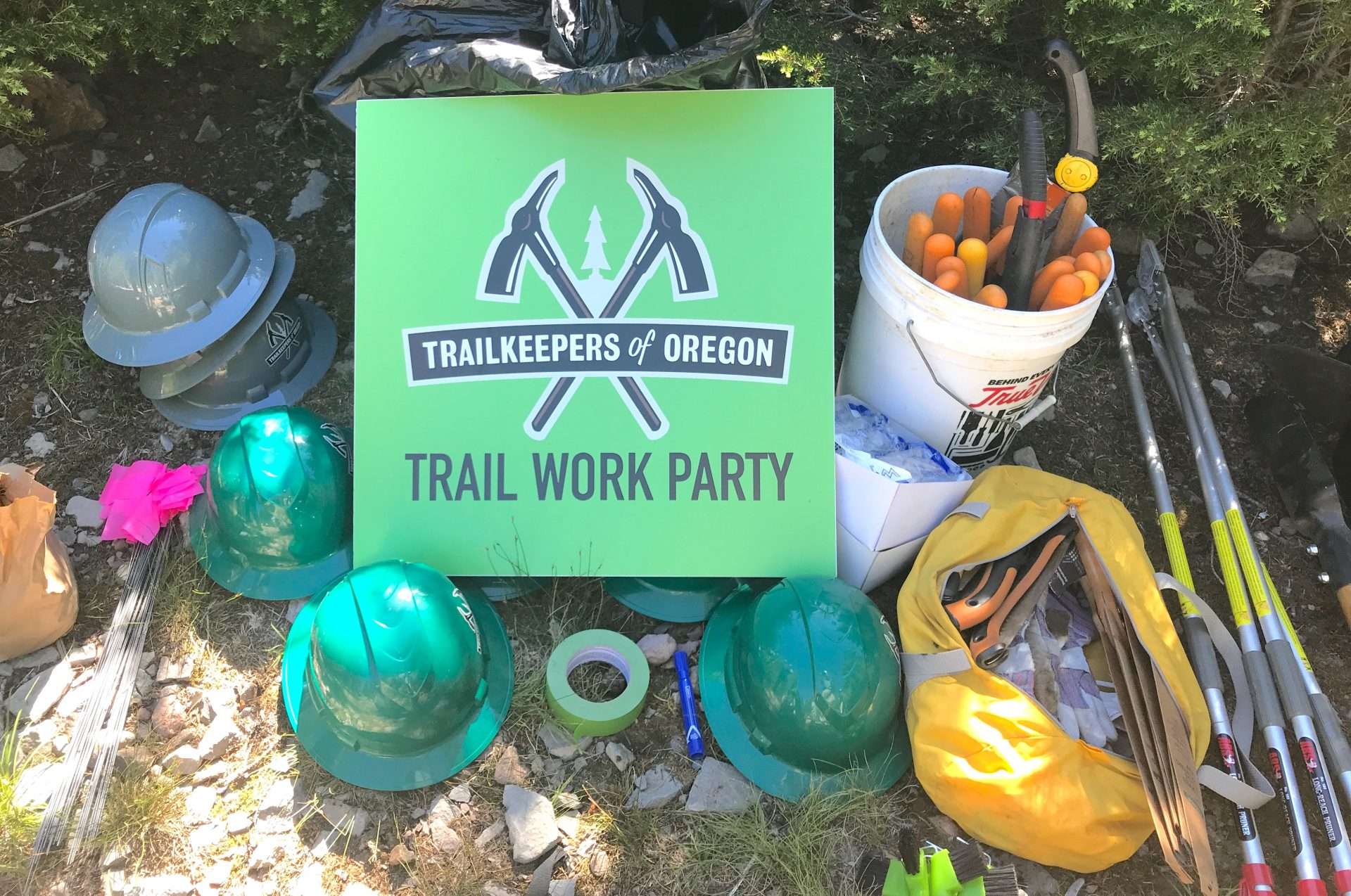 A TKO "Trail Work Party" sign surrounded by hardhats, gloves, loppers, and other trail tools.