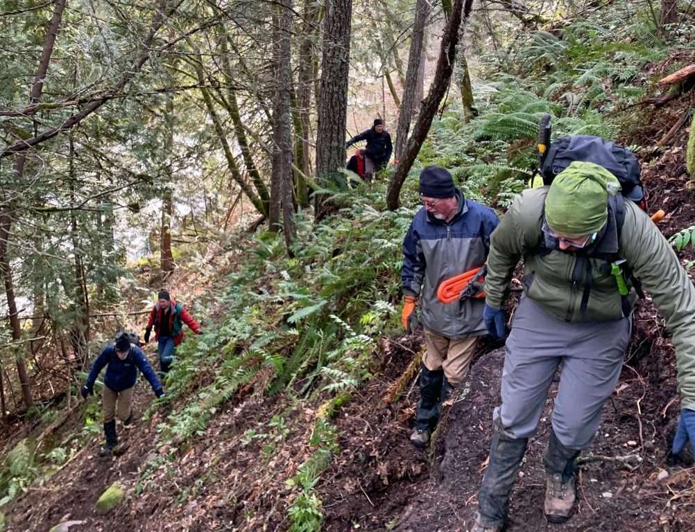A half-dozen hikers spread out on a steep wooded slope.