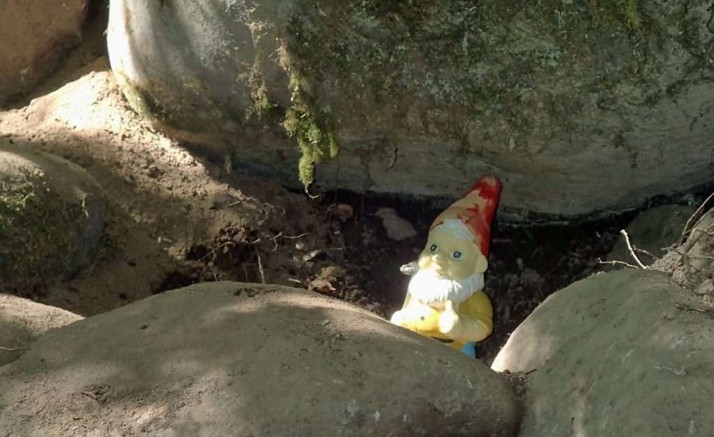 A garden gnome looking out from some boulders.