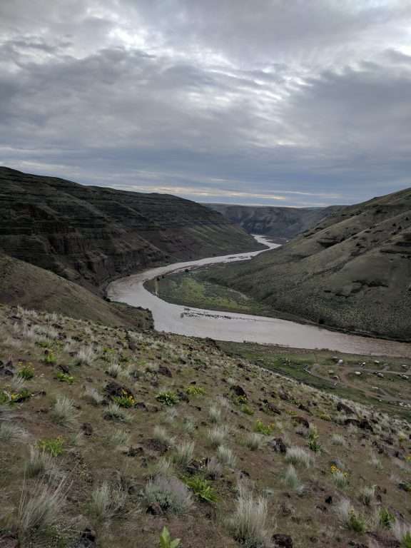 A view looking down on a campground and a river winding through a canyon past treeless grassy slopes.