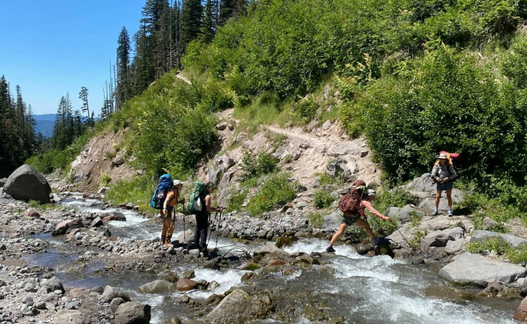 Four backpackers cross a stream