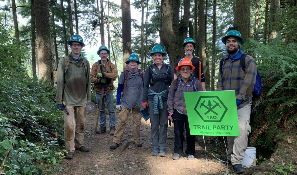 a group of volunteers in hard hats stand smiling on a dirt trail