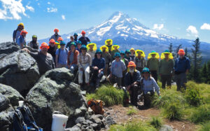 A large group of volunteers poses together in front of Mount Hood.