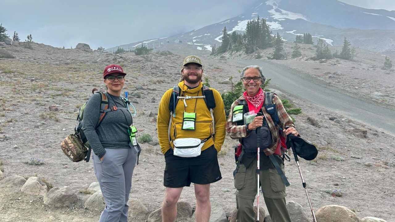 Three Wilderness Ambassadors stand together smiling on trail in front of Mount Hood.