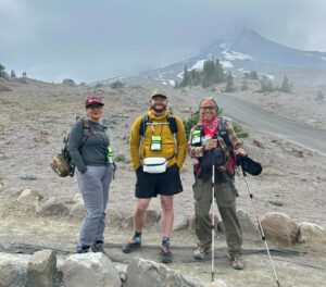 Three volunteer Wilderness Ambassadors stand on trail smiling in front of Mount Hood.