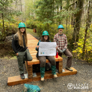 Three volunteers sit on a fully decked August Mountain Trail bridge.