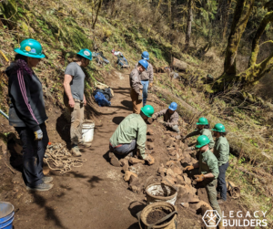 A group of volunteers work to build a rock wall along a trail.