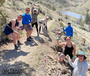 A group of volunteers along a rocky trail overlooking a lake work to improve the trail surface.