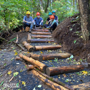 A group of volunteers sit at the top of a newly constructed set of wooden stairs.