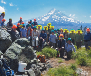 A large group of volunteers pose together at Owl Point with Mount Hood looming in the background.