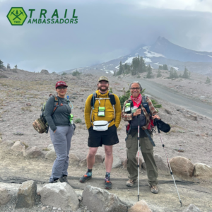 Three TKO Wilderness Ambassadors stand on trail in front of Mount Hood.